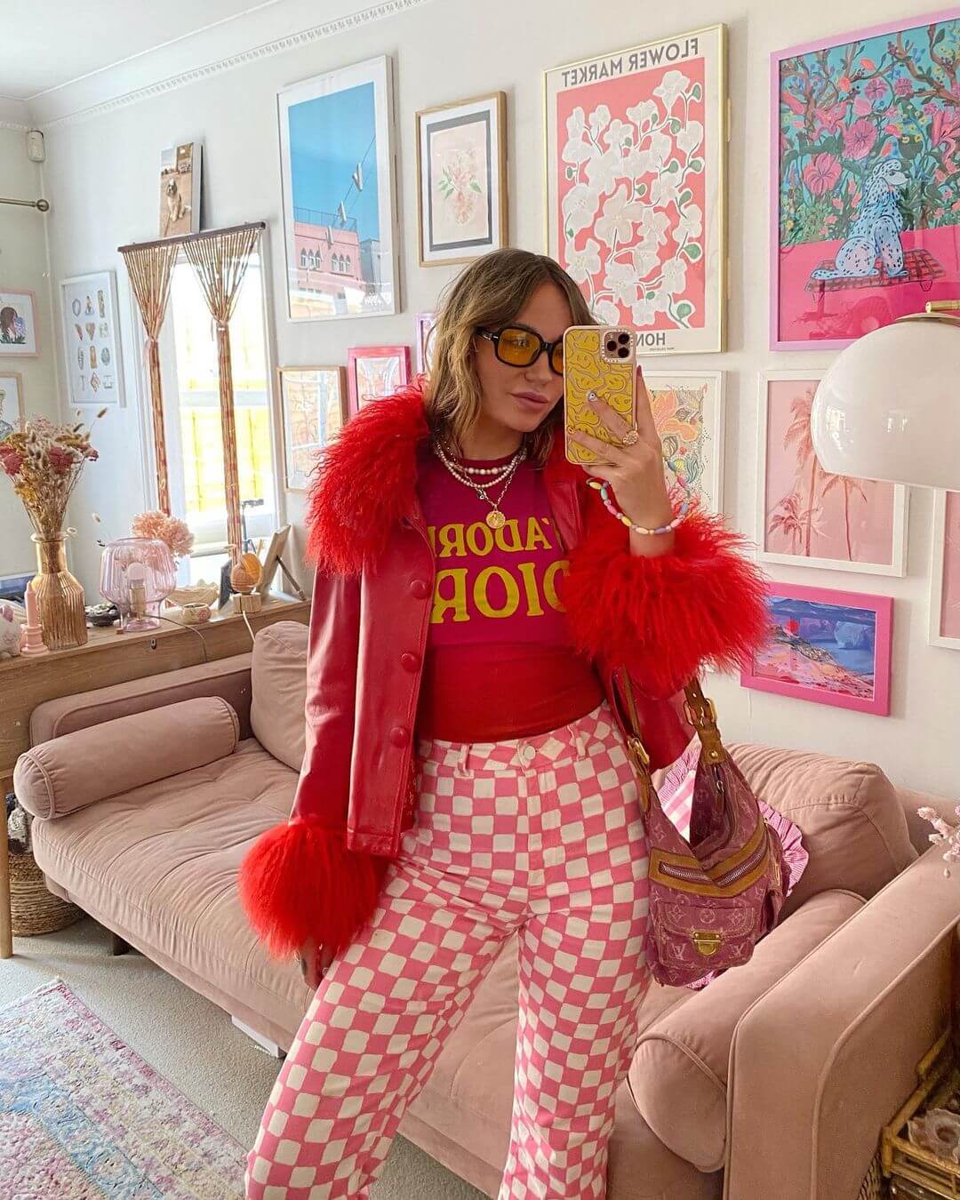 Sara Waiste wearing a red fur trimmed leather jacket, dior t-shirt and pink and white checkerboard trousers