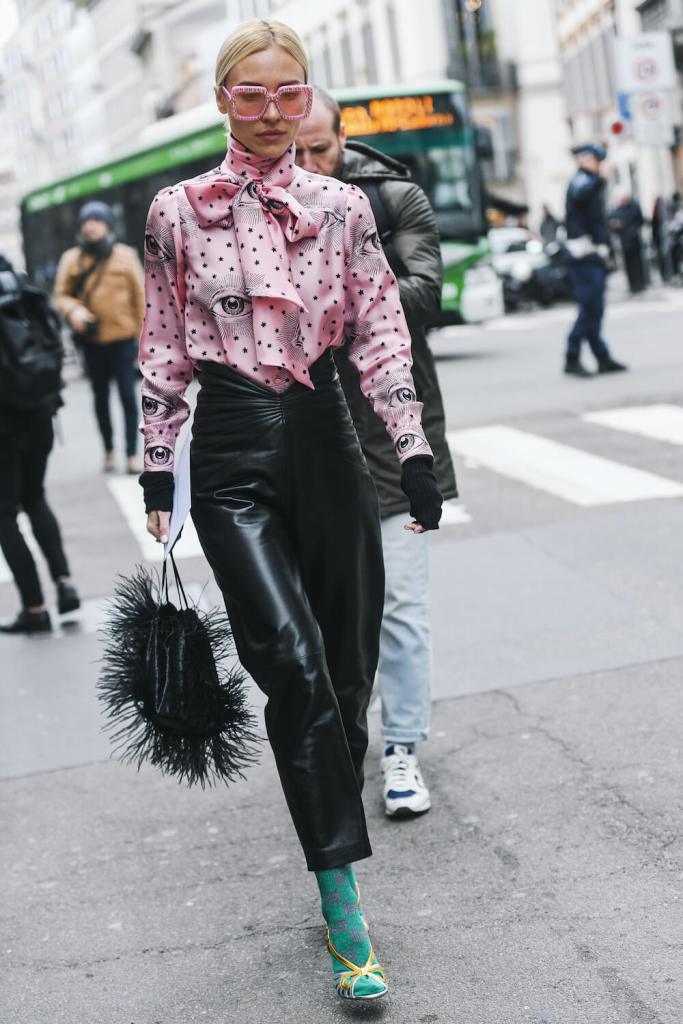 Woman at Milan Fashion Week wears pink pussybow blouse, leather trousers, Gucci socks, heels and a feather bag