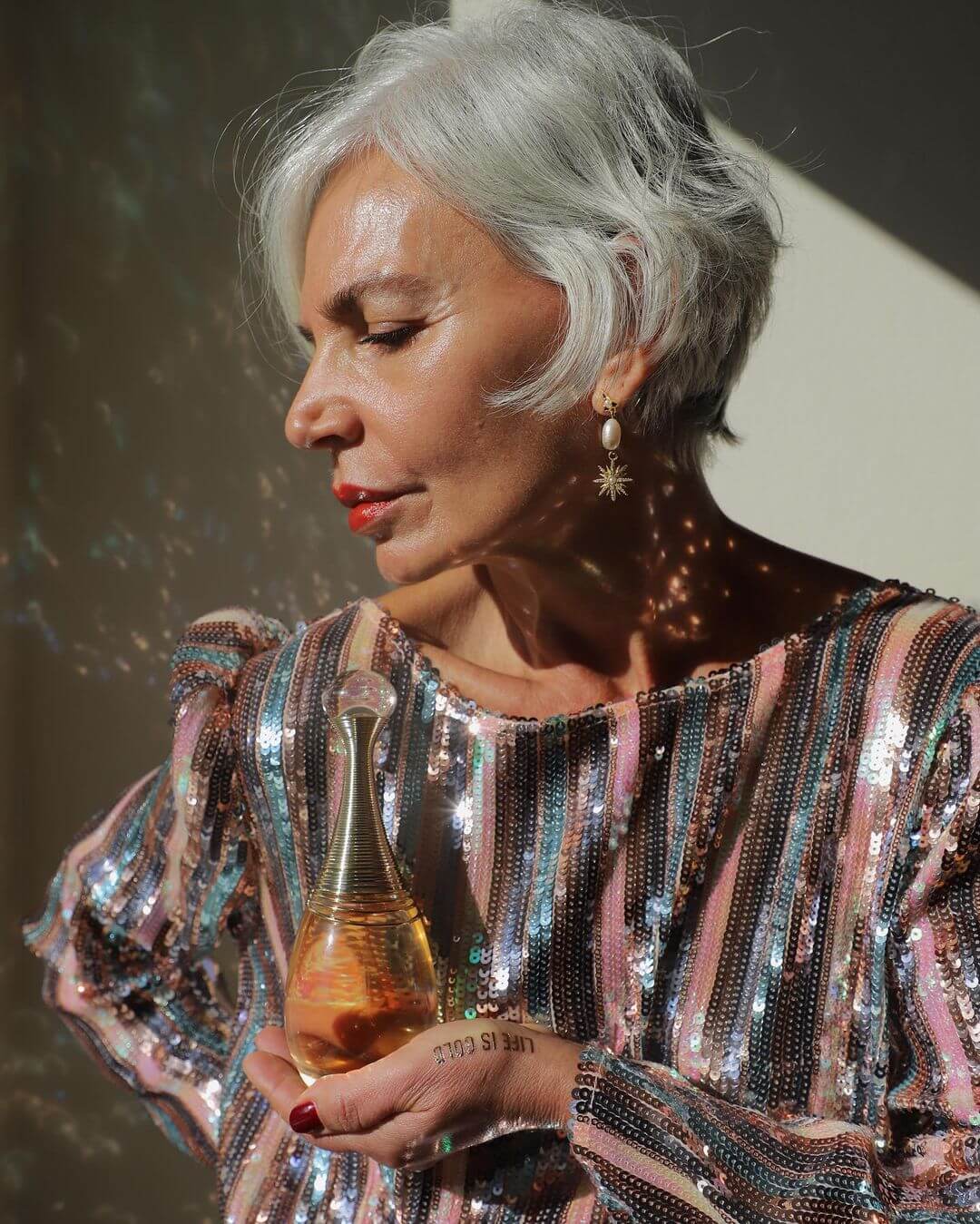grece ghanem wearing a sequin top and holding a bottle of perfume