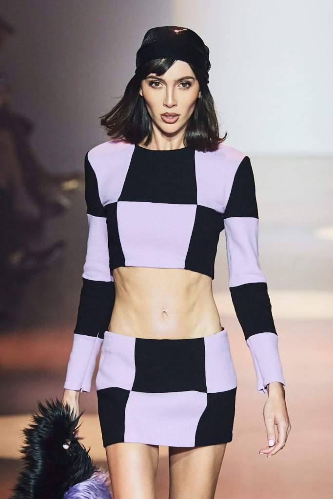Model wears purple and black checkerboard mini skirt and long-sleeve top on Cowan SS22 catwalk 
