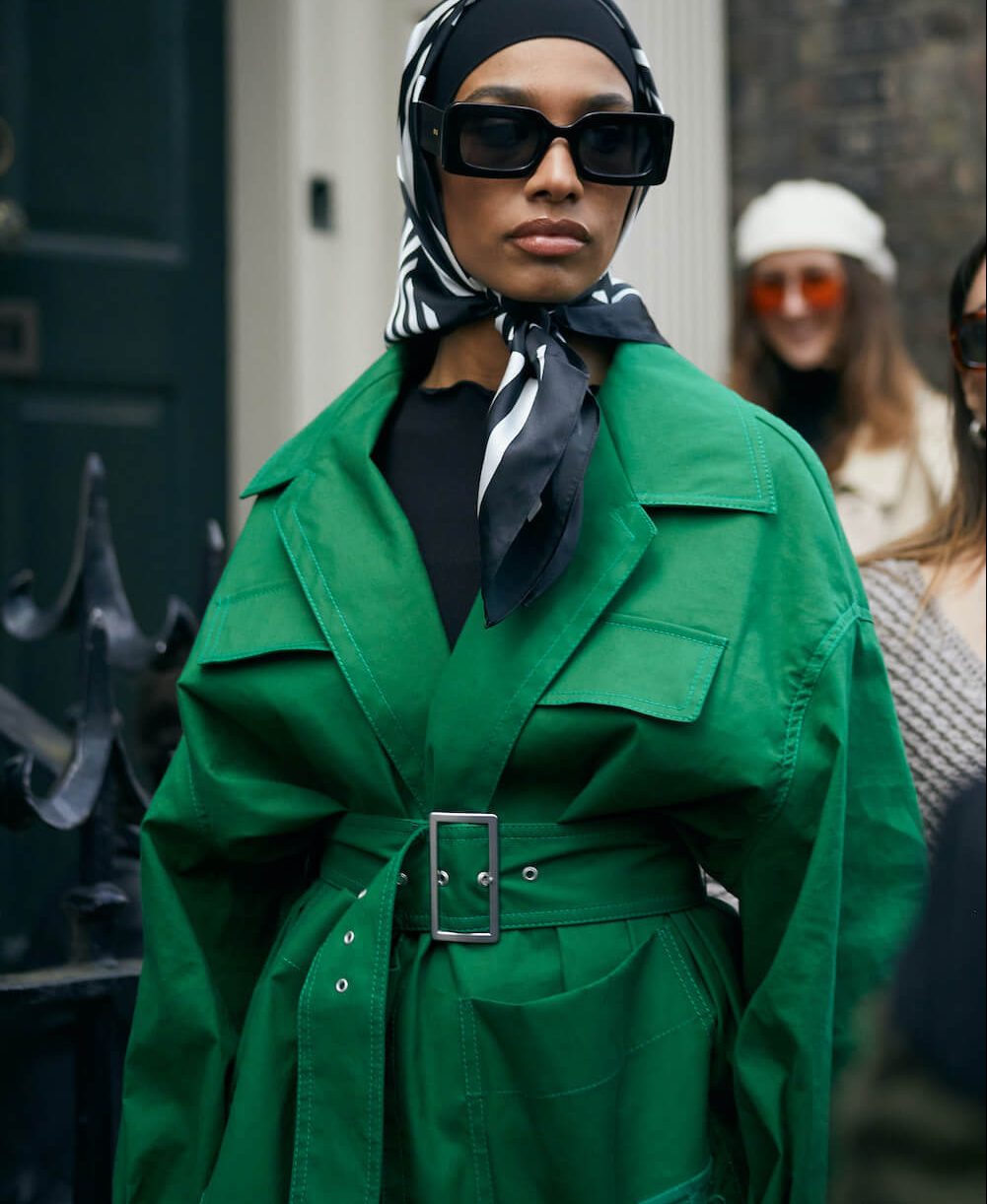 woman wears head scarf and green trench coat at london fashion week