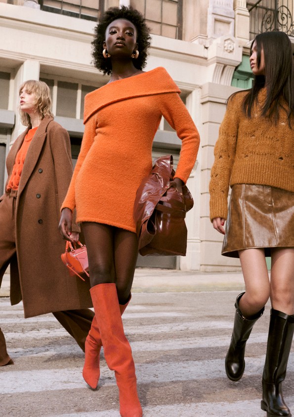 H&M autumn winter campaign showing a black woman wearing an orange jumper dress and orange knee-high boots
