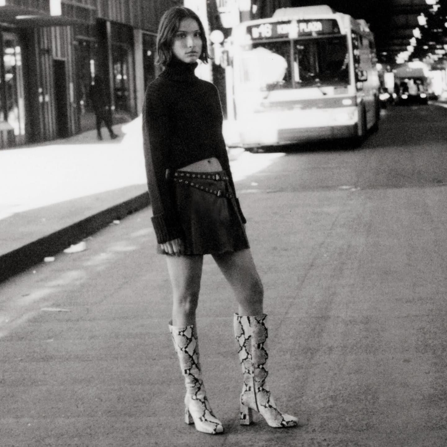 Woman wears Zara black sweater, leather mini skirt and snakeskin boots in black and white photograph 